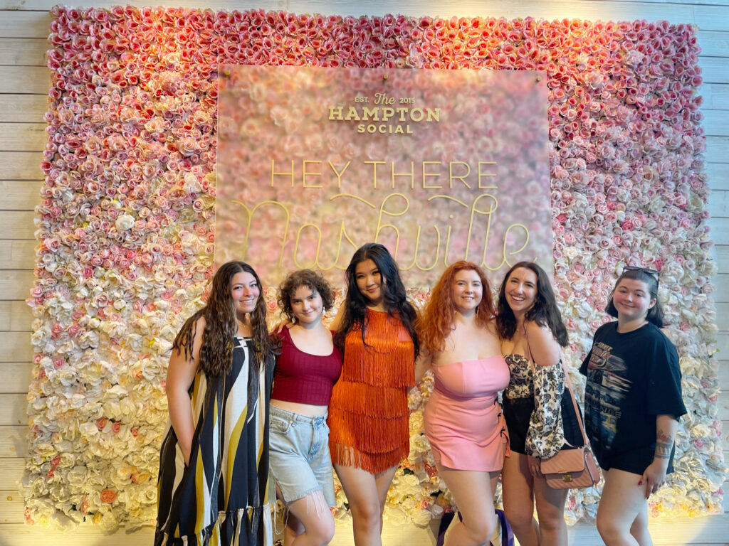 6 friends smiling in front of a pink floral wall in nashville