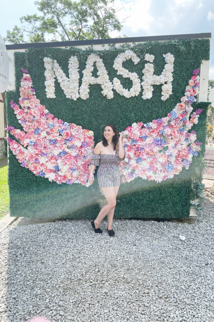 girl in a floral dress smiling in front of a floral installation in the shape of wings in nashville