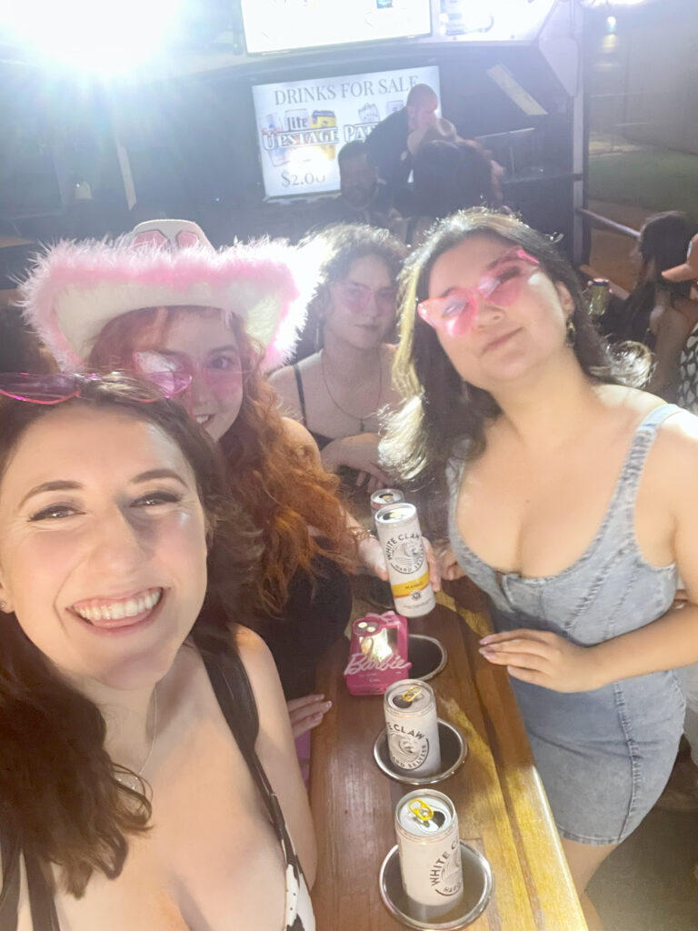 4 friends smiling at the camera with pink heart shaped sunglasses on, standing in a party bus in nashville