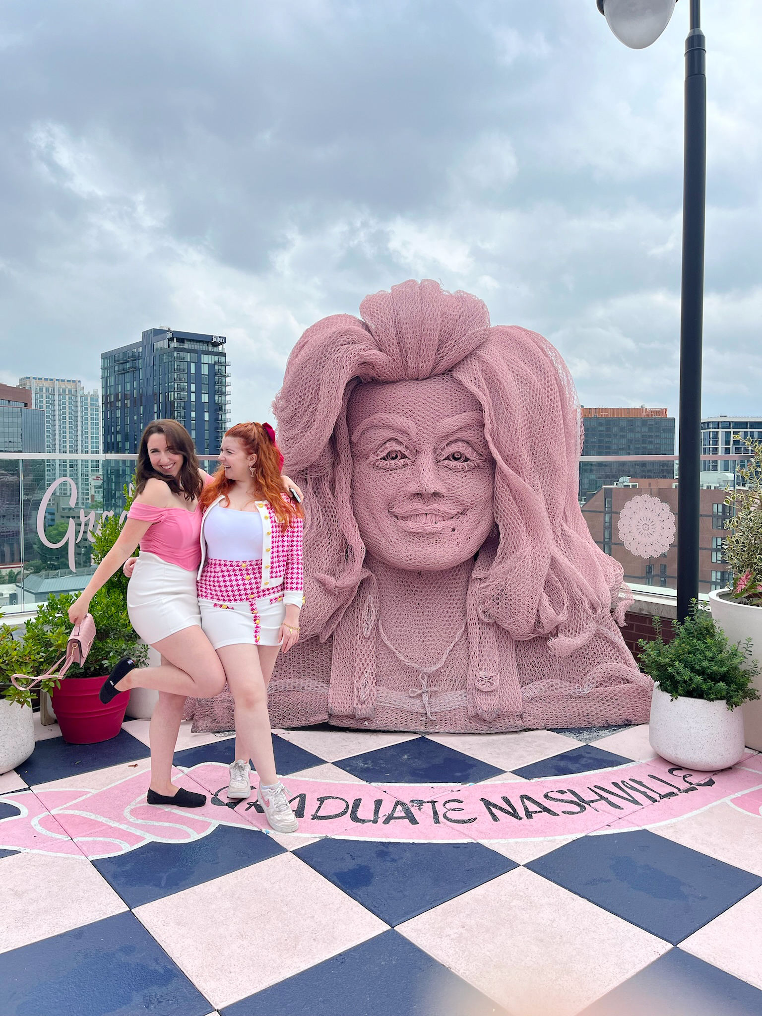 two friends on a bachelorette or birthday party smiling in front of a pink statue of dolly partons head at the white limozeen resteraunt in nashville