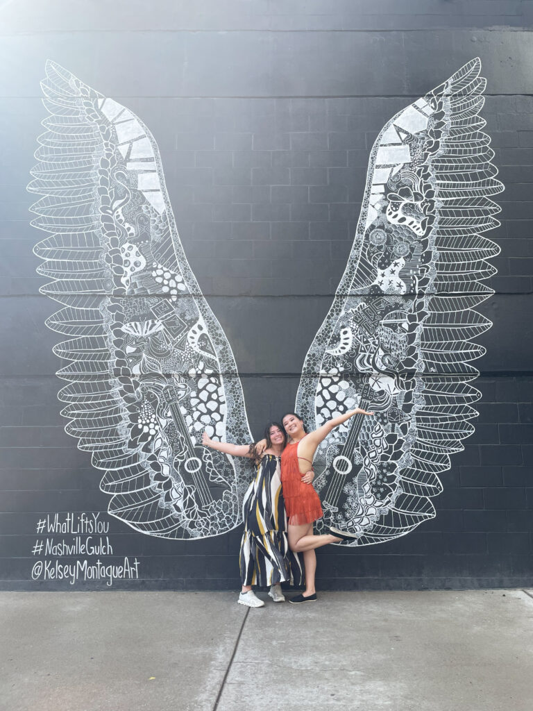 two girls smiling in front of a mural of wings on a bachelorette trip in nashville