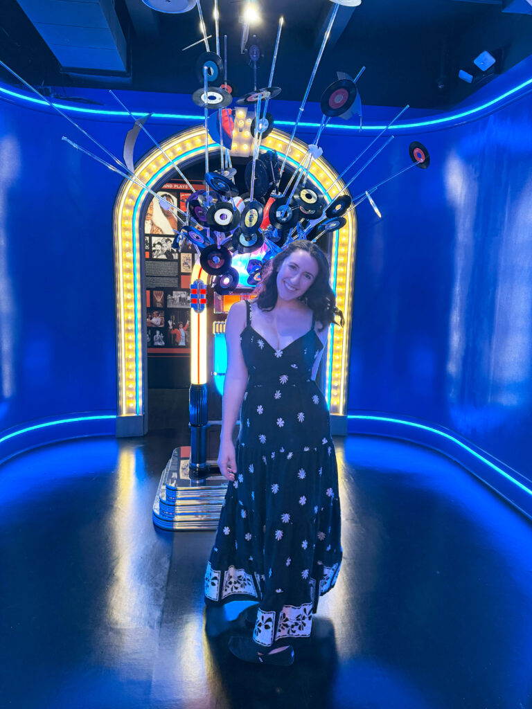 a girl in a black dress standing in front of a set at the musuem of broadway