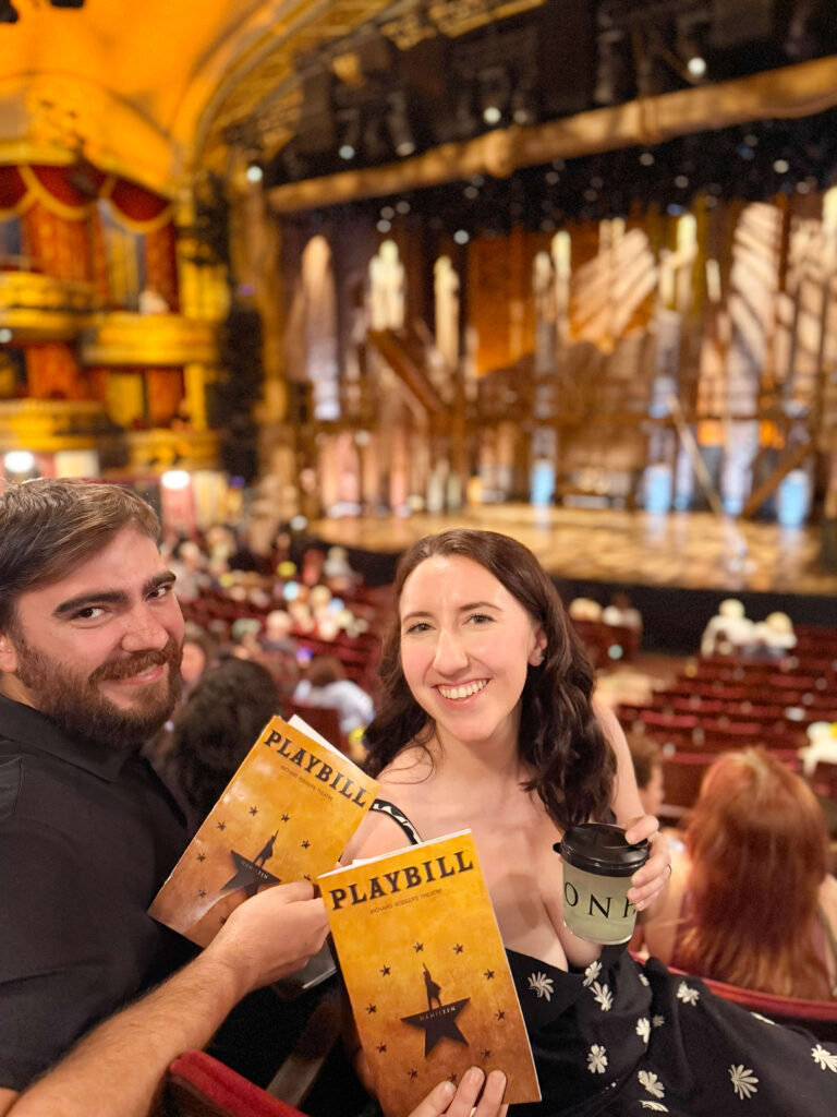 a man and wife smiling in the audience at the hamilton broadway show