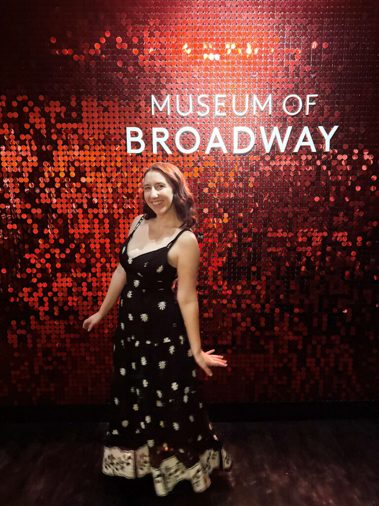 a woman in a black dress standing in front of a sign that says museum of broadway